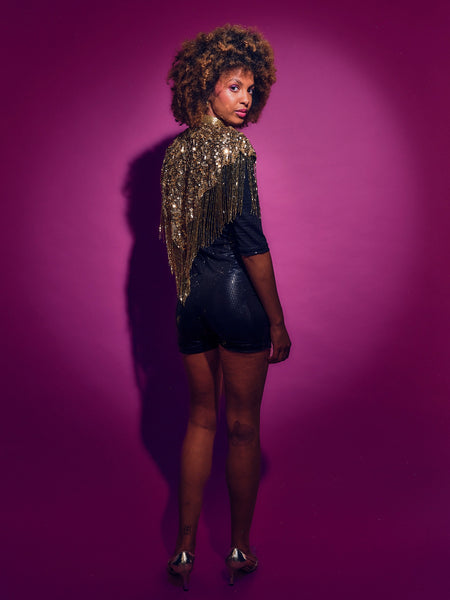 Woman wearing a sequined top and black shorts against a purple background