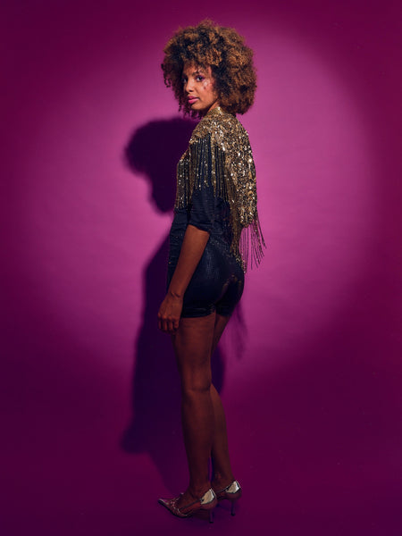 Person wearing a black outfit with gold accents against a purple background
