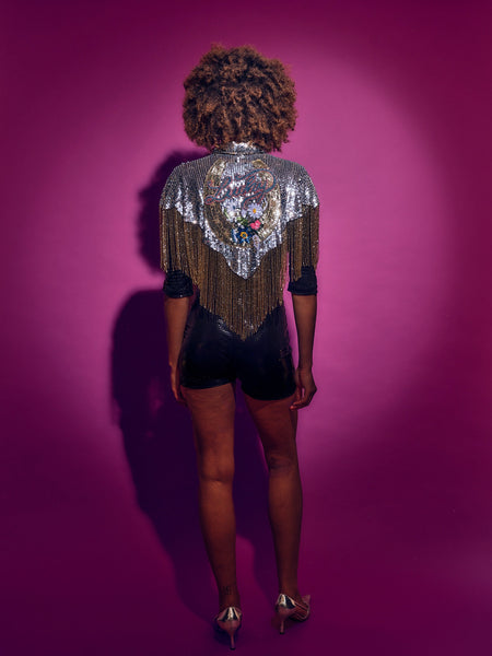 Person wearing a sequinned Cape and black shorts against a pink background
