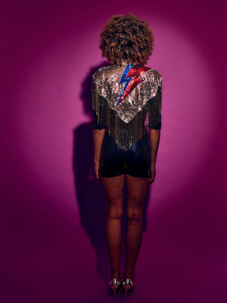 Person wearing a sequined top with a colorful design on a purple background