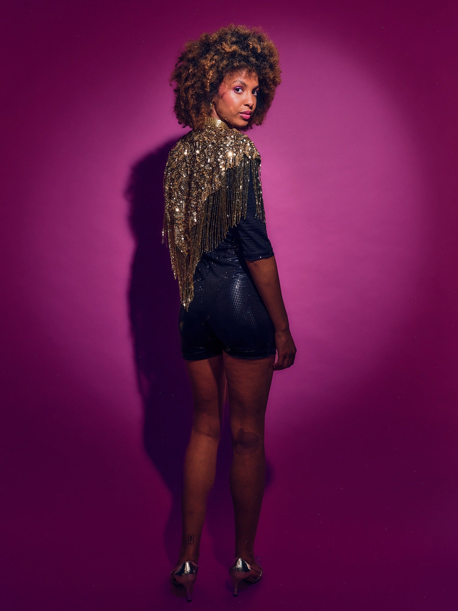 Woman wearing a sequined top and black shorts against a purple background