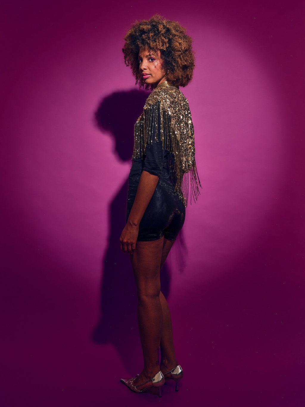 Person wearing a black outfit with gold accents against a purple background