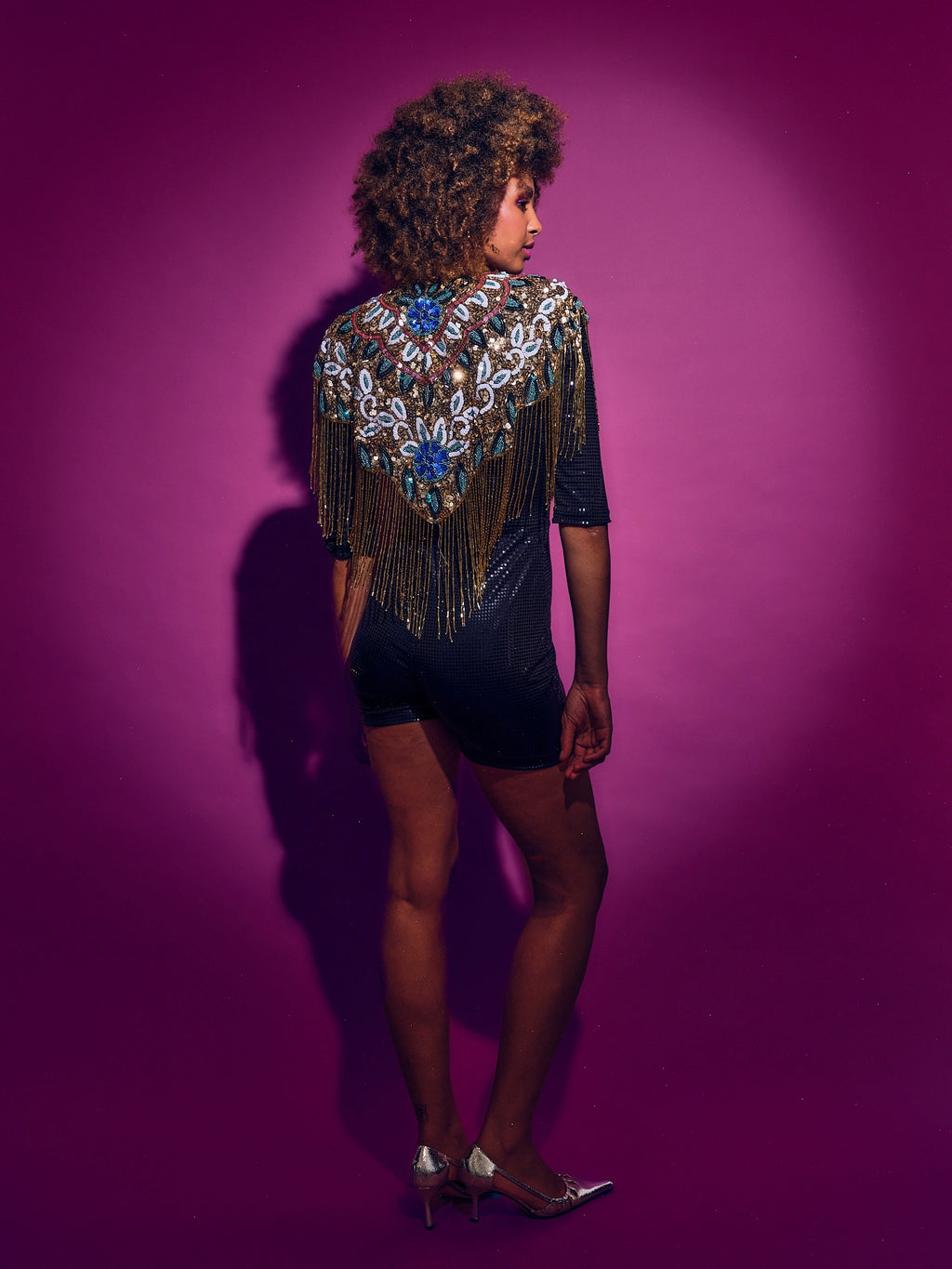 Person wearing a sparkling top with fringe and sequins against a purple background