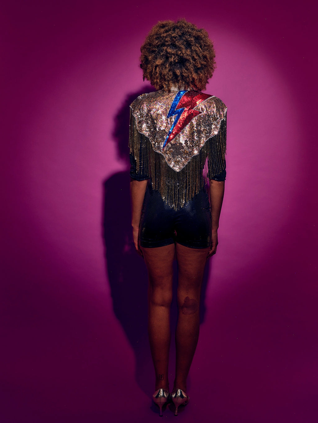Person wearing a sequined top with a colorful design on a purple background