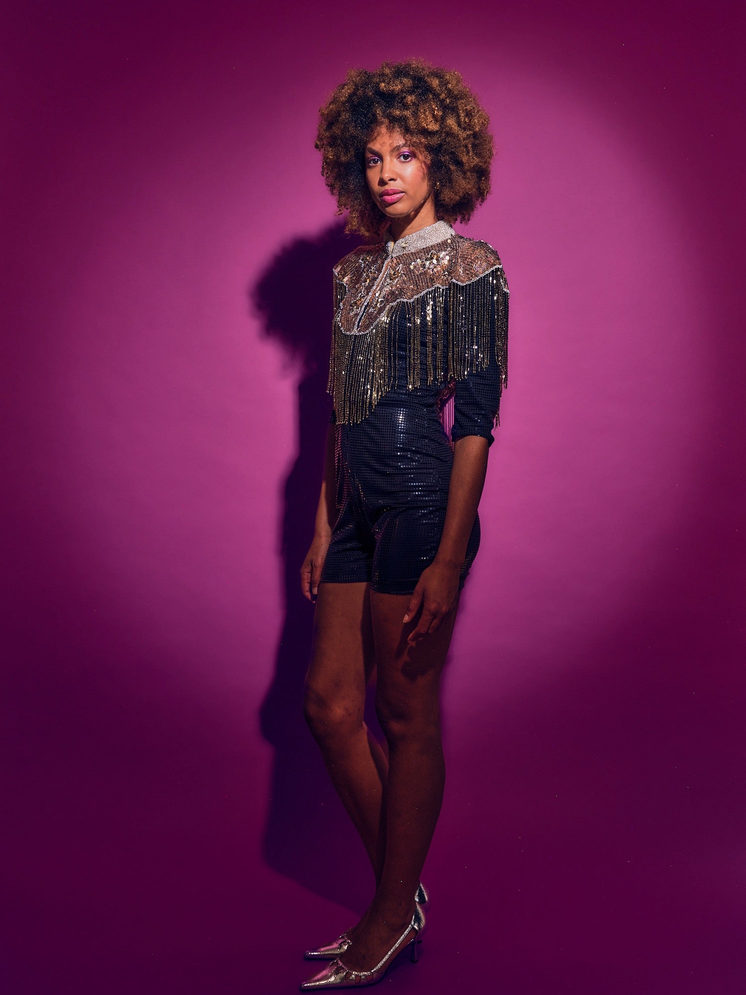 Person wearing a black outfit with gold embellishments against a purple background