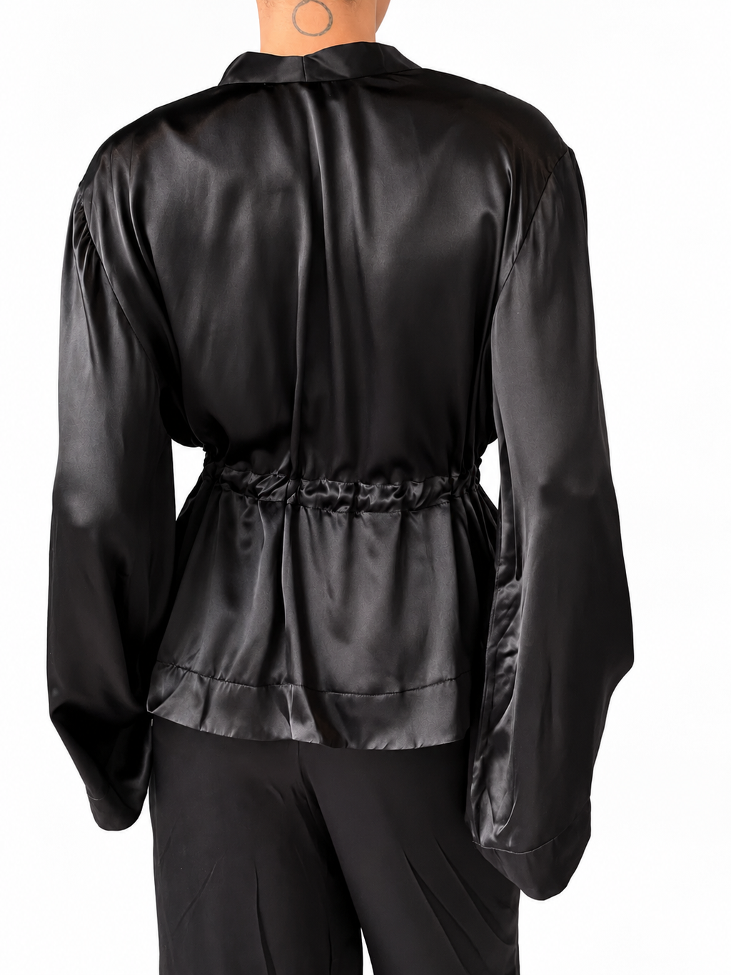 A person shown from the back wearing a black satin or silky long-sleeve top with a gathered waist and black pants, against a plain white studio background.